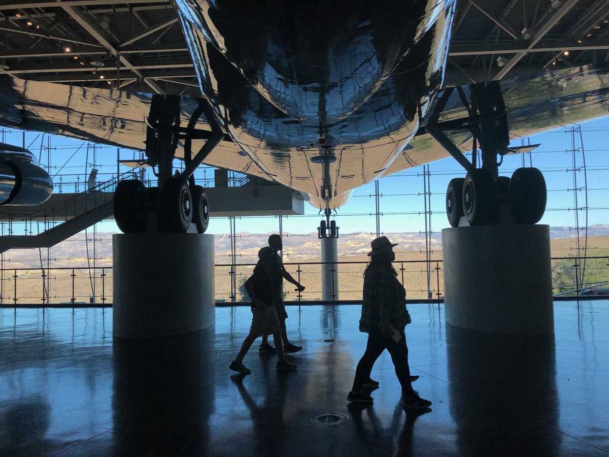 A small group of people walking in the shadow of a jet propped up for display