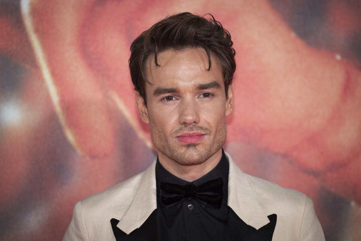 Liam Payne looks serious and not too happy in a black-and-whit tux jacket over a black shirt