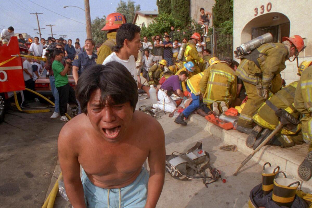 A man cries on the street, with firefighters behind him