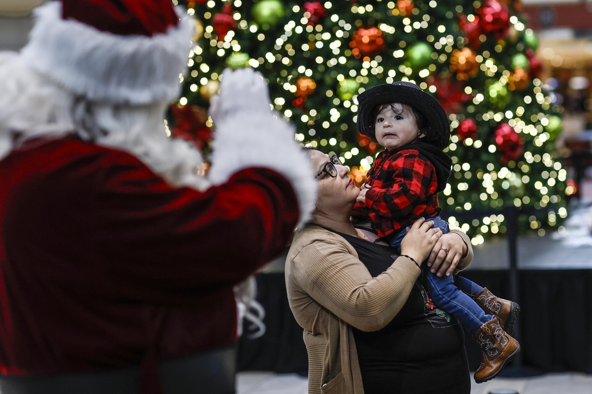 Adan Gonzalez is carried by his mother, Anjelica, to a Santa Claus photo spot at the Puente Hills Mall.