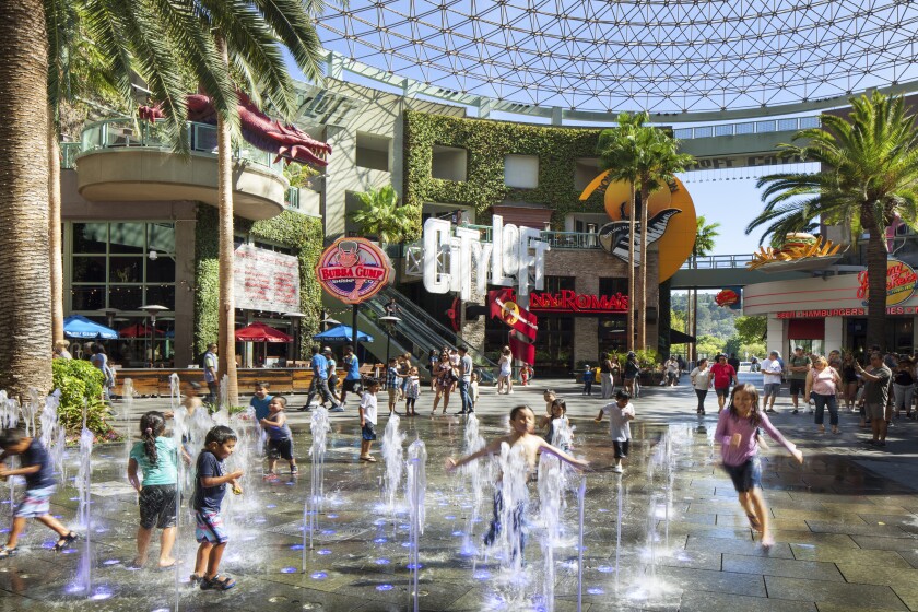 Children play in a fountain area surrounded by shops in a circular plaza covered by a glass roof.