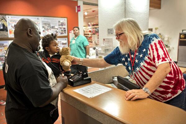 Rodney Edwards, left, and his son Nigel are greeted at the front desk at San Francisco General by volunteer Thomas DiBell. The hospital is one of many working to improve the patient experience, prompted by healthcare reform that ties federal payments to patient satisfaction.