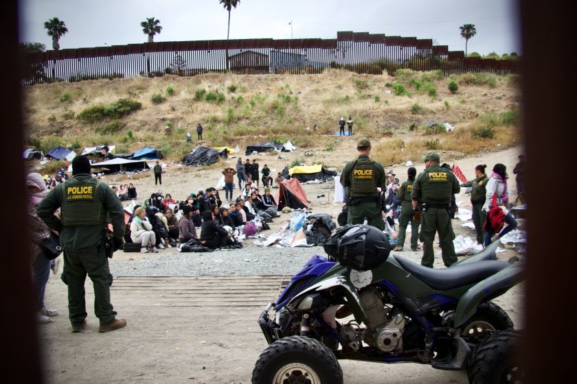Migrants wait at the border between the fences separating Tijuana and San Diego.