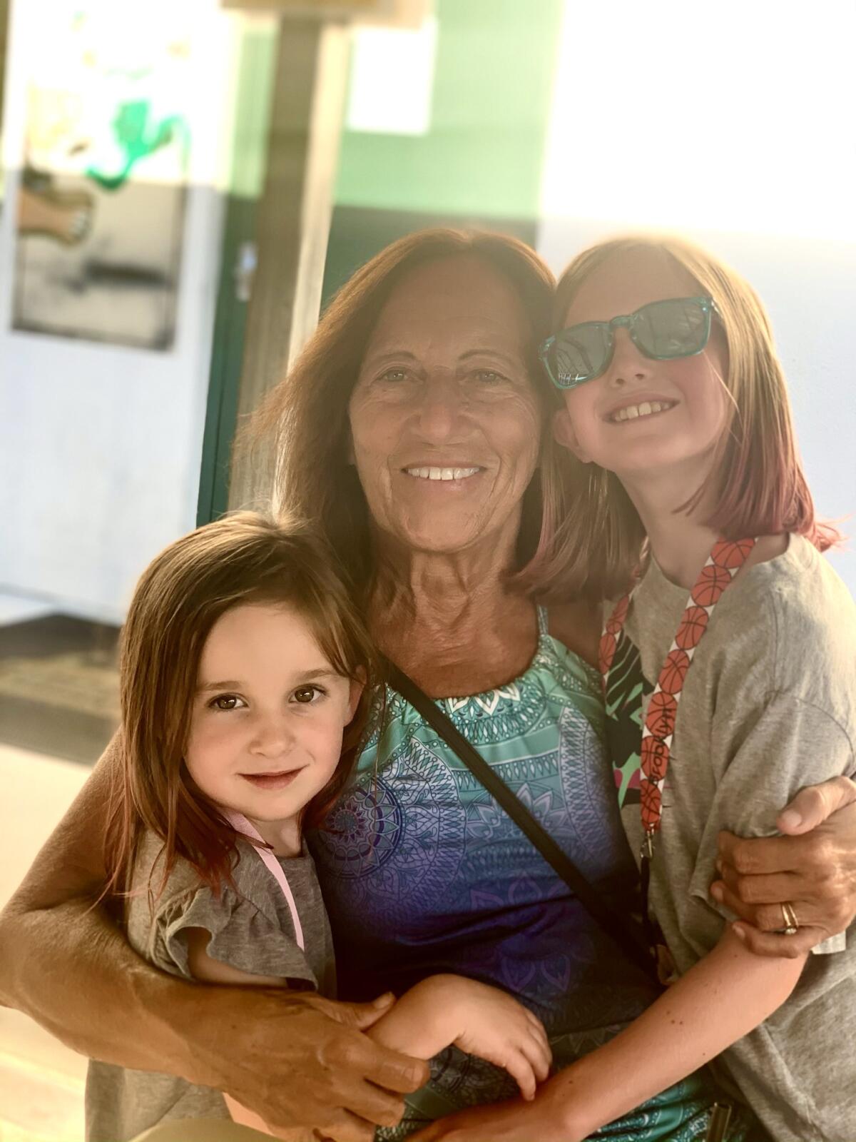 A woman and her granddaughters pose for a photo.