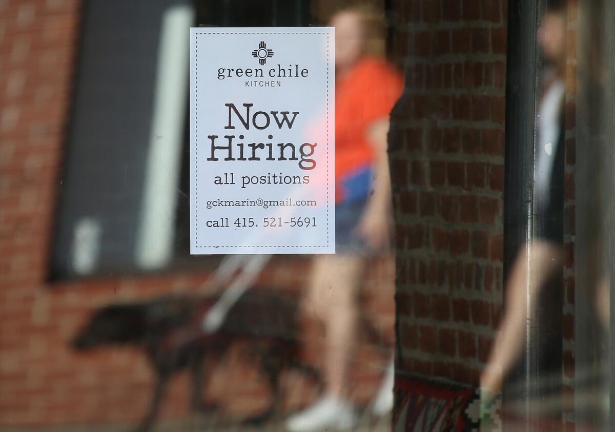 Pedestrians walk by a "Now Hiring" sign posted in a store window of a business in San Rafael, Calif., on Nov. 7.