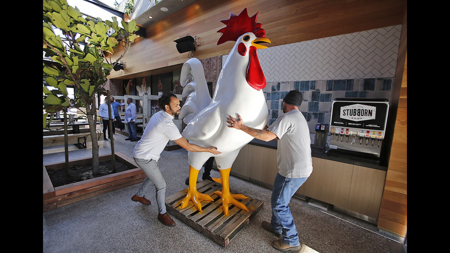 Costa Mesa general manager Renaldo Robinson, left, helps a worker move the giant chicken mascot into place at the new Crack Shack location in Costa Mesa.