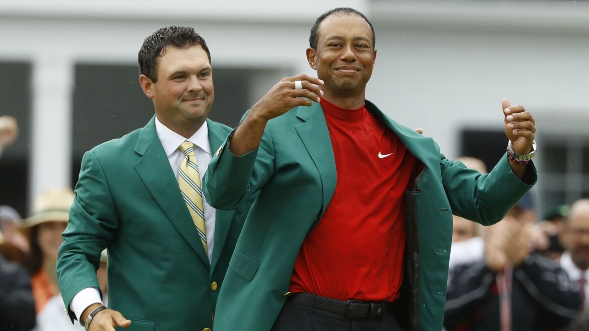 Patrick Reed helps Tiger Woods put on his green jacket after Woods won the Masters on Sunday.