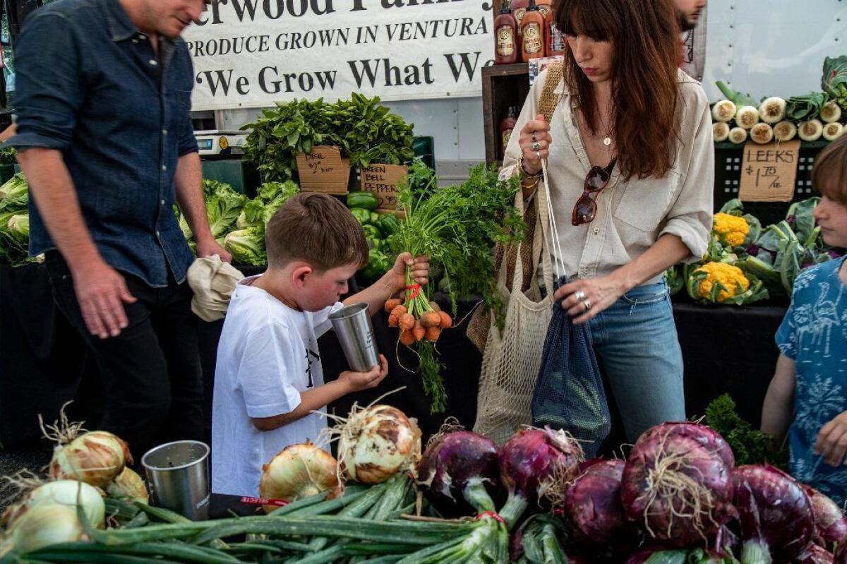 James ayuda a sus padres, Jasper y Vjera Watts, a comprar verduras orgánicas con su hermana Isla, de 8 años, a la derecha, en el Farmers Market de Altadena.