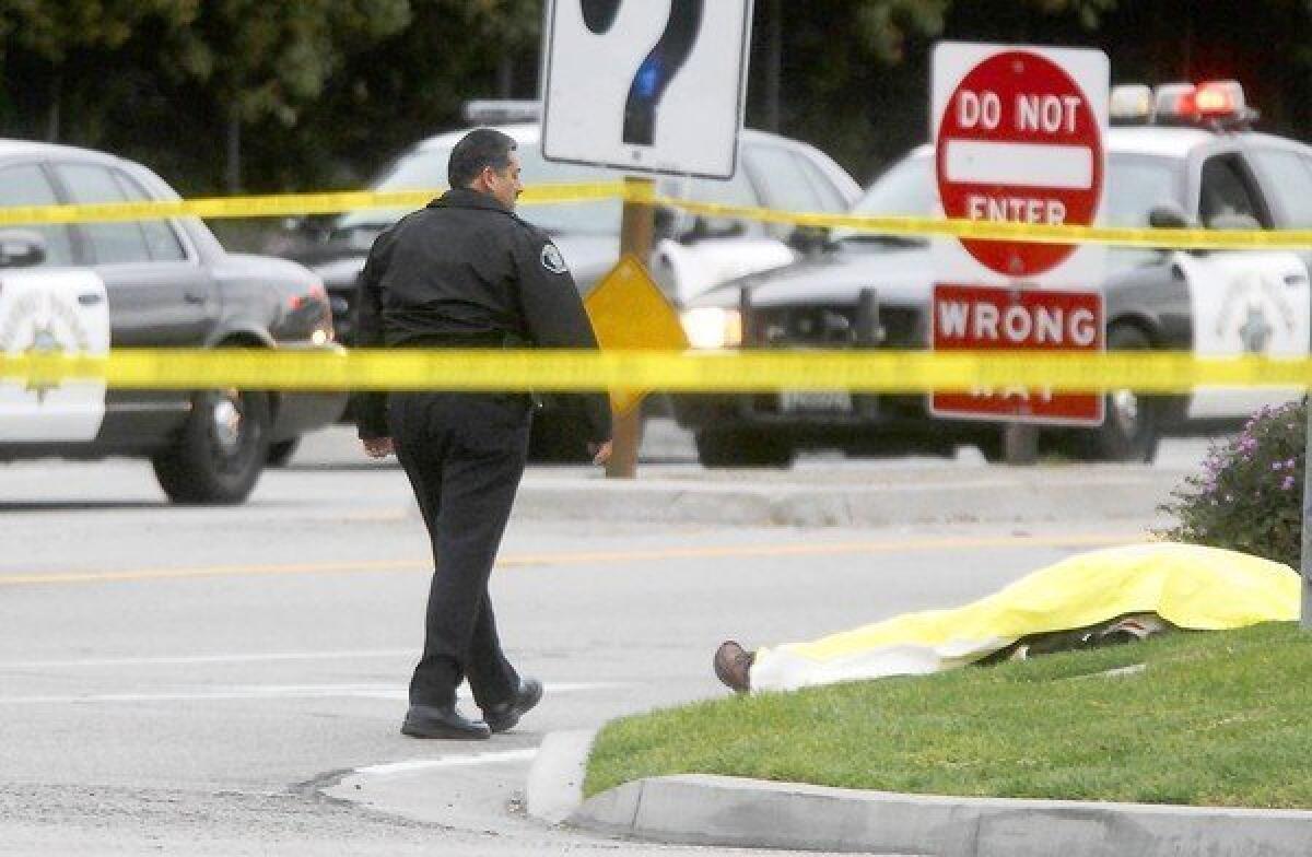 A Santa Ana police officer walks by the body of a victim shot at the Edinger Avenue off-ramp from the southbound 55 Freeway. Authorities say Ali Syed shot six people, three fatally, before killing himself.