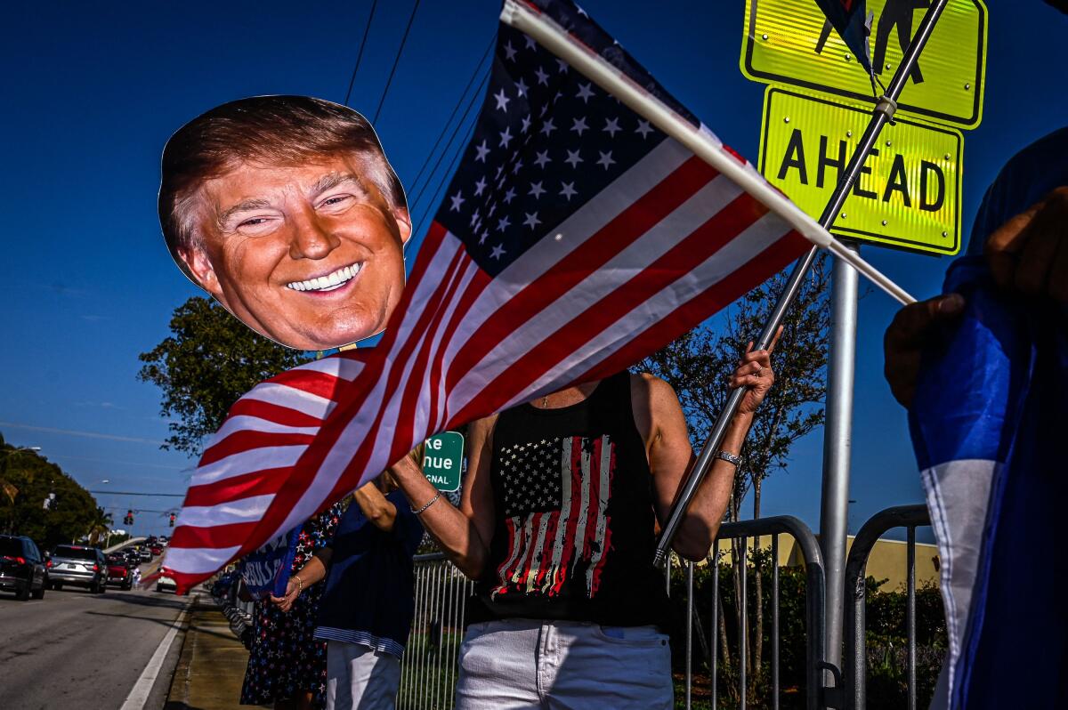A cutout of President Trump's head and an American flag are held by his supporters on a road side.