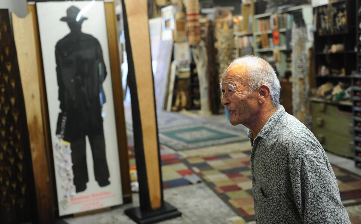 Kenzi Shiokava walks through a tidy passageway in his studio that is flanked with artistic objects.