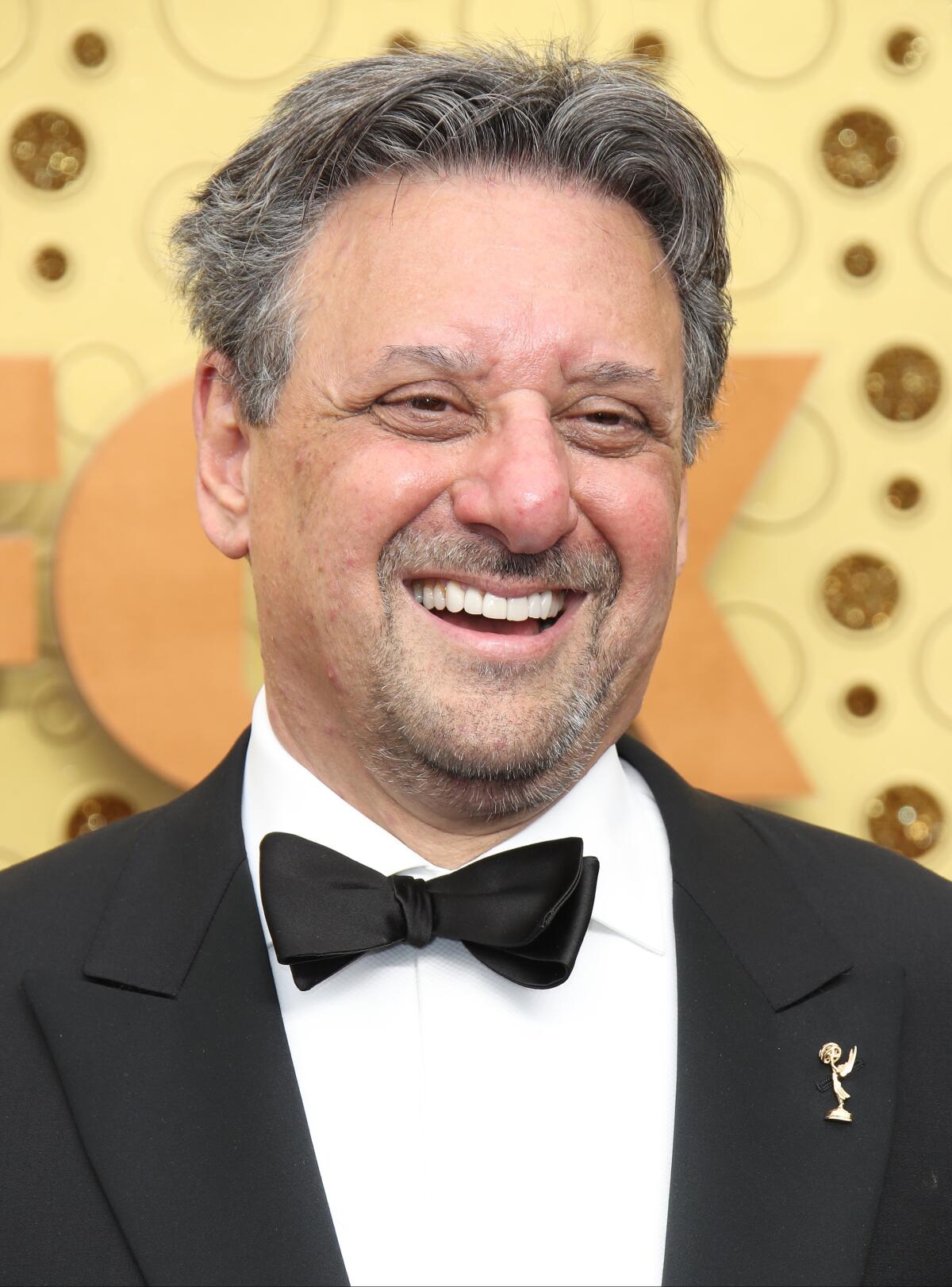 A smiling man at an awards ceremony wearing an Emmy pin