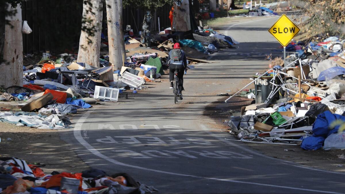 A bicyclist rides past piles of trash left at a Santa Ana River homeless encampment after more than 700 people were relocated from the Anaheim site in February.