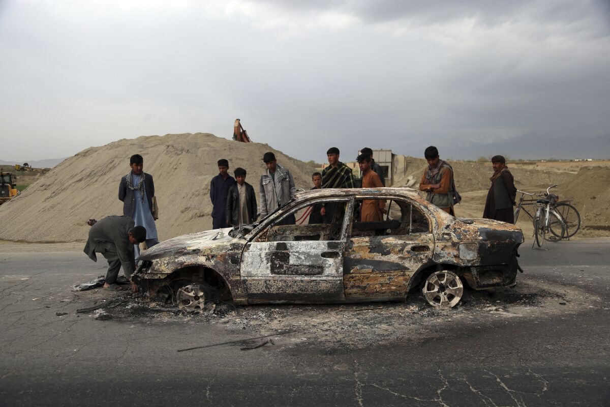 FILE - In this April 9, 2019, file photo, Afghans watch a civilian vehicle burnt after being shot by U.S. forces following an attack near the Bagram Air Base, north of Kabul, Afghanistan. Three American service members and a U.S. contractor were killed when their convoy hit a roadside bomb on Monday near the main U.S. base in Afghanistan, the U.S. forces said. The Taliban claimed responsibility for the attack. Intelligence alleging that Afghan militants might have accepted Russian bounties for killing American troops didn’t scuttle the U.S.-Taliban agreement or President Donald Trump’s plan to withdraw thousands more troops from the war. (AP Photo/Rahmat Gul, File)