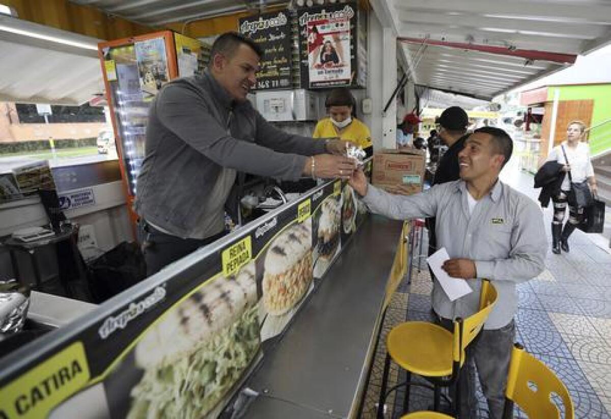 En esta imagen del 11 de junio de 2019, Gerson Briceño, propietario del restaurante de comida rápida "Arepas Cafe", sirve a un cliente en Bogotá, Colombia, el martes 11 de junio de 2019. (AP Foto/Fernando Vergara)