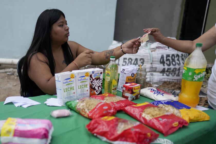 Janet, who works for the social movement Dignity, waits on a customer from behind a table offering food staples at lower prices than offered at the supermarkets, amid rising inflation, in Buenos Aires, Argentina, Thursday, March 16, 2023. (AP Photo/Natacha Pisarenko)