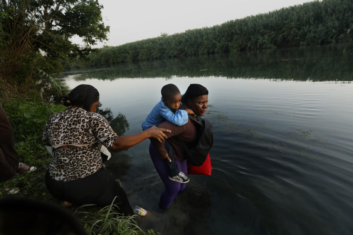 Two women enter the Rio Grande River, one carrying a child on her back and one in her arms, not visible, as they try to reach the United States. (Carolyn Cole/Los Angeles Times)