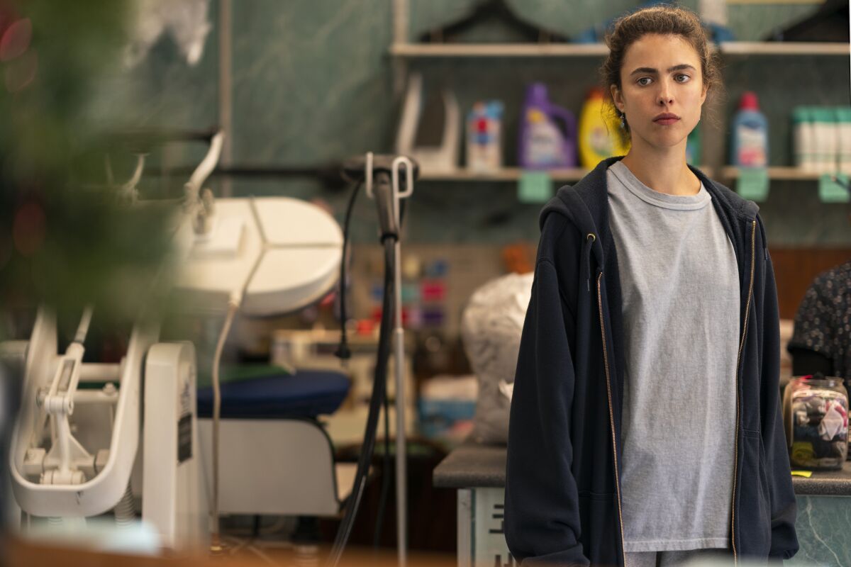 A casually dressed woman standing in a cluttered room.