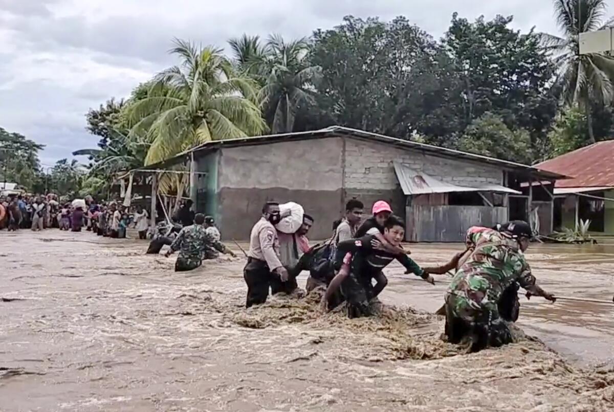 Soldiers and police officers help residents cross a flooded road in Malaka Tengah, Indonesia.