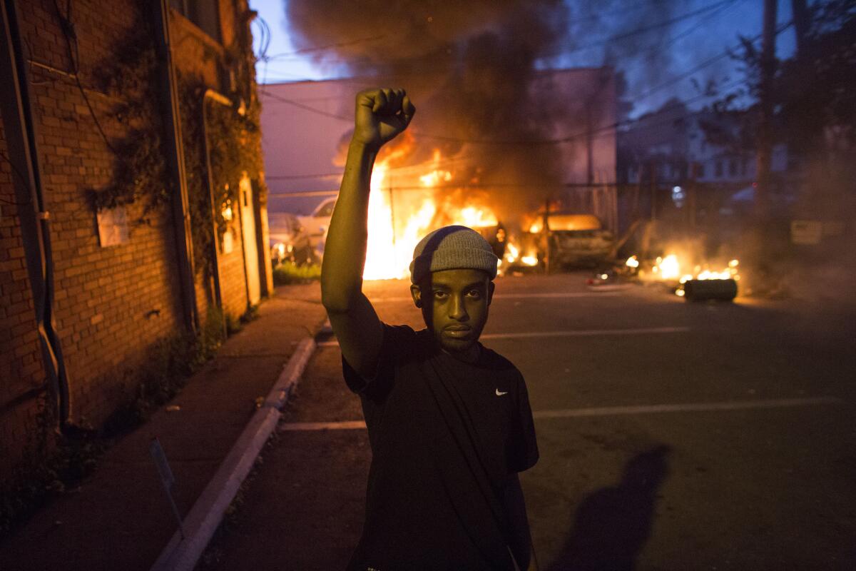 A protester holds a fist in the air in front of a burning car lot in Minneapolis on Friday night.