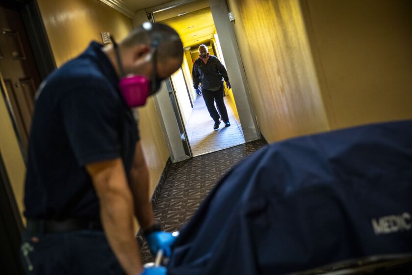 WEST COVINA, CA - OCTOBER 13: Kristina McGuire, an investigator with Los Angeles County Dept. of Medical Examiner-Coroner walks toward Jerry Meza, forensic attendant, to help move the gurney carrying the lifeless body of Judy Bounthong, 58, an ob-gyn tech who died of coronavirus complications, at the Days Inn by Wyndham, in West Covina, CA, on Tuesday, Oct. 13, 2020. Bounthong, who worked at Emanate Queen of the Valley Hospital, died near the end of her isolation period, she wasn't discovered for several days. (Jay L. Clendenin / Los Angeles Times)