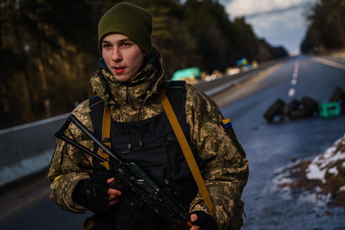 A soldier in a knit cap and military fatigues holds a weapon 