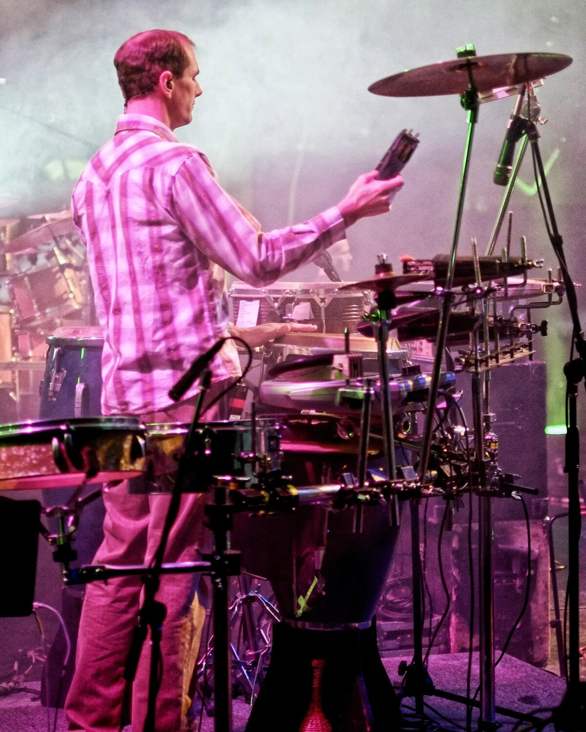 A person stand behind a drum set.