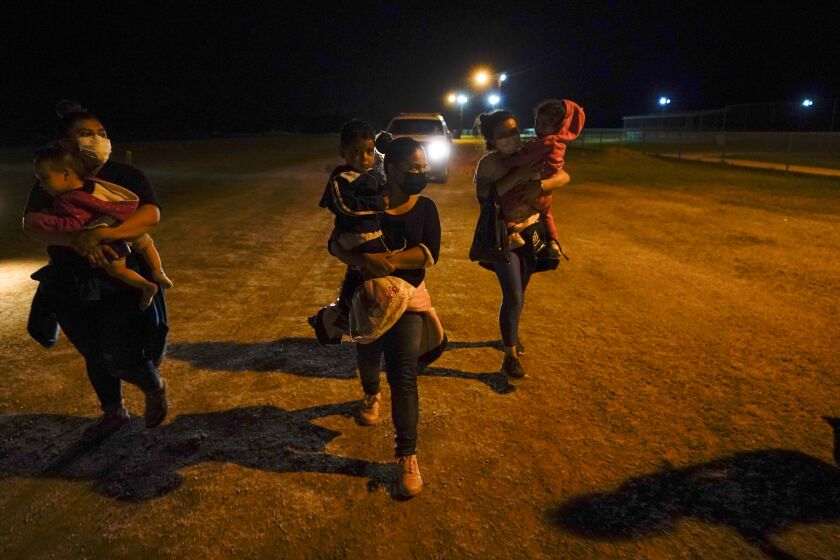 FILE - In this May 11, 2021, file photo, migrant women carry children in the rain at an intake area after turning themselves in upon crossing the U.S.-Mexico border in La Joya, Texas. The U.S. Homeland Security Department says thousands of asylum-seekers whose claims were dismissed or denied under a Trump administration policy that forced them to wait in Mexico for their court hearings will be allowed to return for another chance at humanitarian protection. The Associated Press has learned that registration begins Wednesday, June 23, 2021 for asylum-seekers who were subject to the “Remain in Mexico” policy and either had their cases dismissed or denied for failing to appear in court. (AP Photo/Gregory Bull, File)