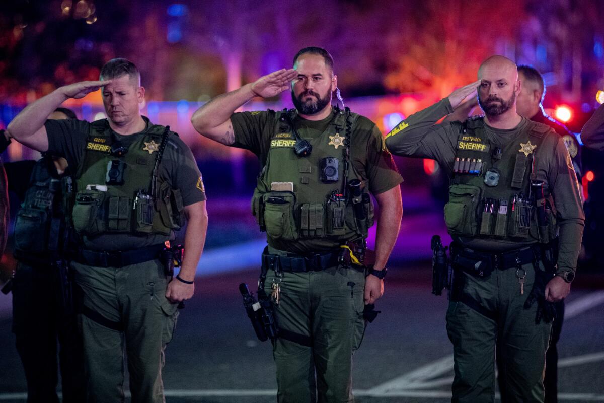 Officers standing in a row salute on a street at night.