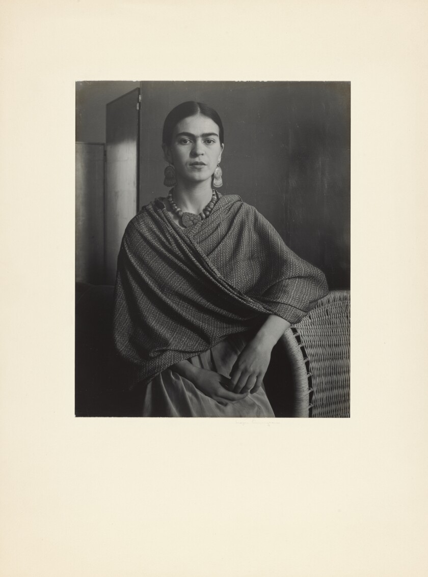Frida Kahlo leans against a wicker chair in a vintage photo by Imogen Cunningham that shows her wearing a rebozo.