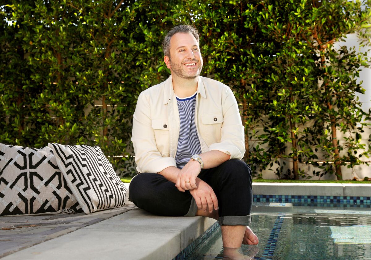 "Bridgerton" creator Chris Van Dusen sits at the edge of a swimming pool with his feet in the water.