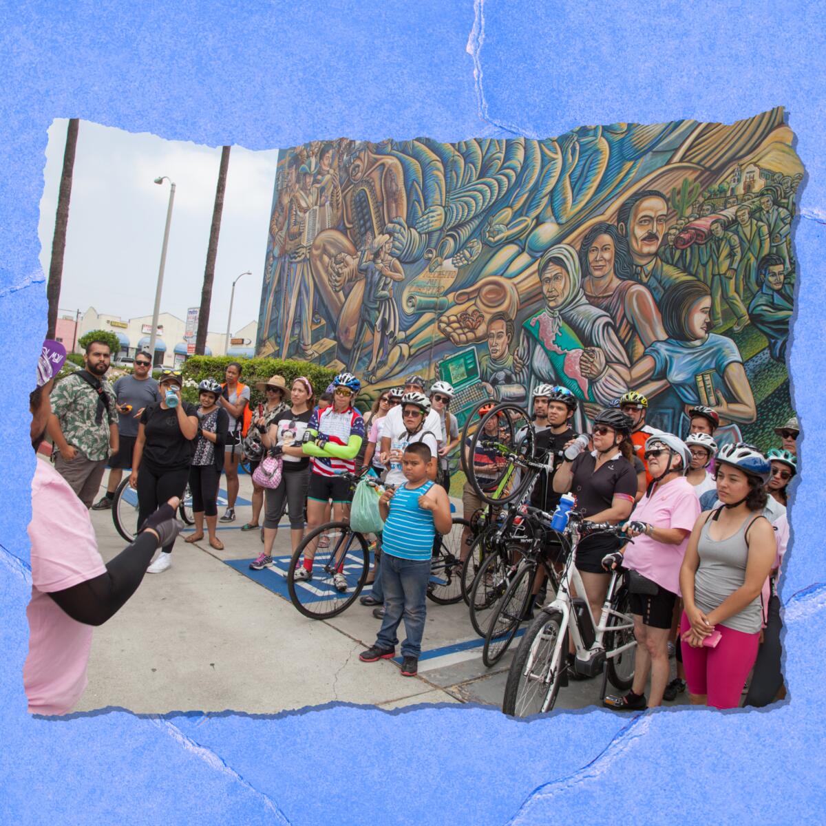 People with bikes stand in front of a large outdoor mural.