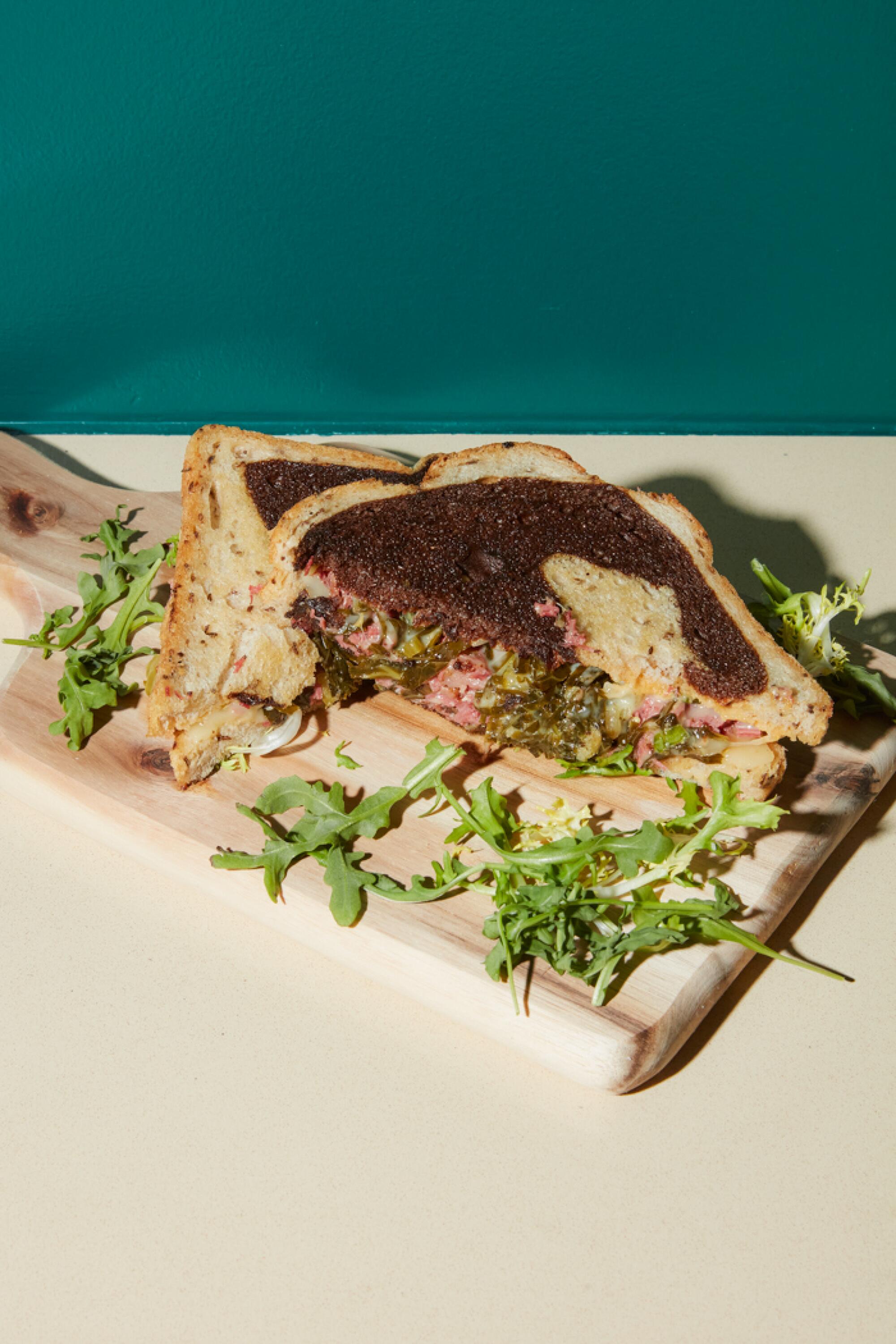 A pastrami sandwich on marbled rye against a green wall