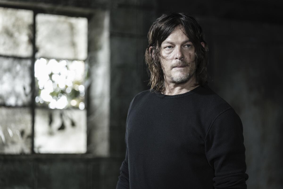 Norman Reedus as Daryl Dixon in 'The Walking Dead' standing in front of a window wearing a black long-sleeve shirt