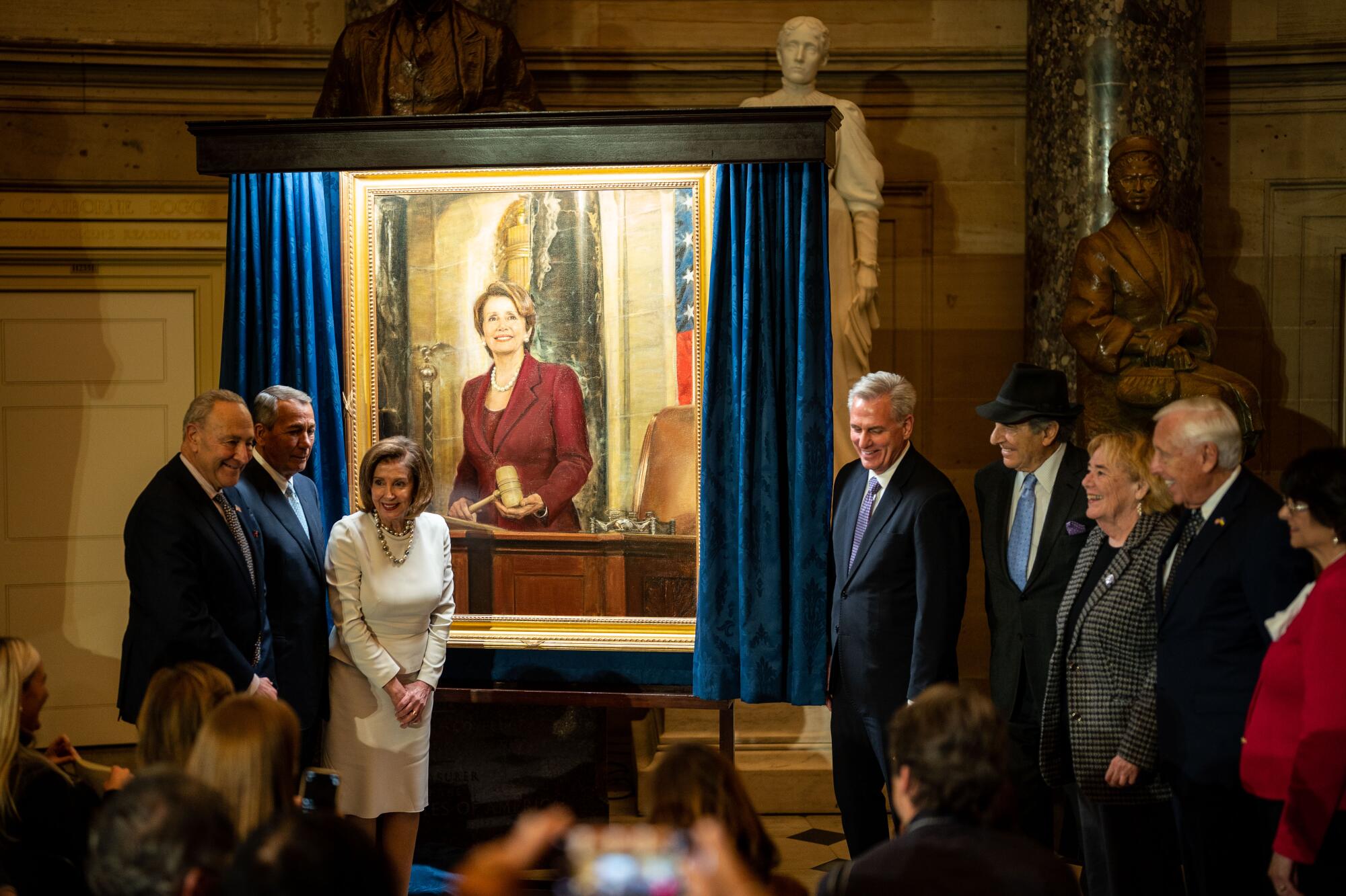 Speaker of the House Nancy Pelosi poses for photos with others near a painting of her in an ornate room.