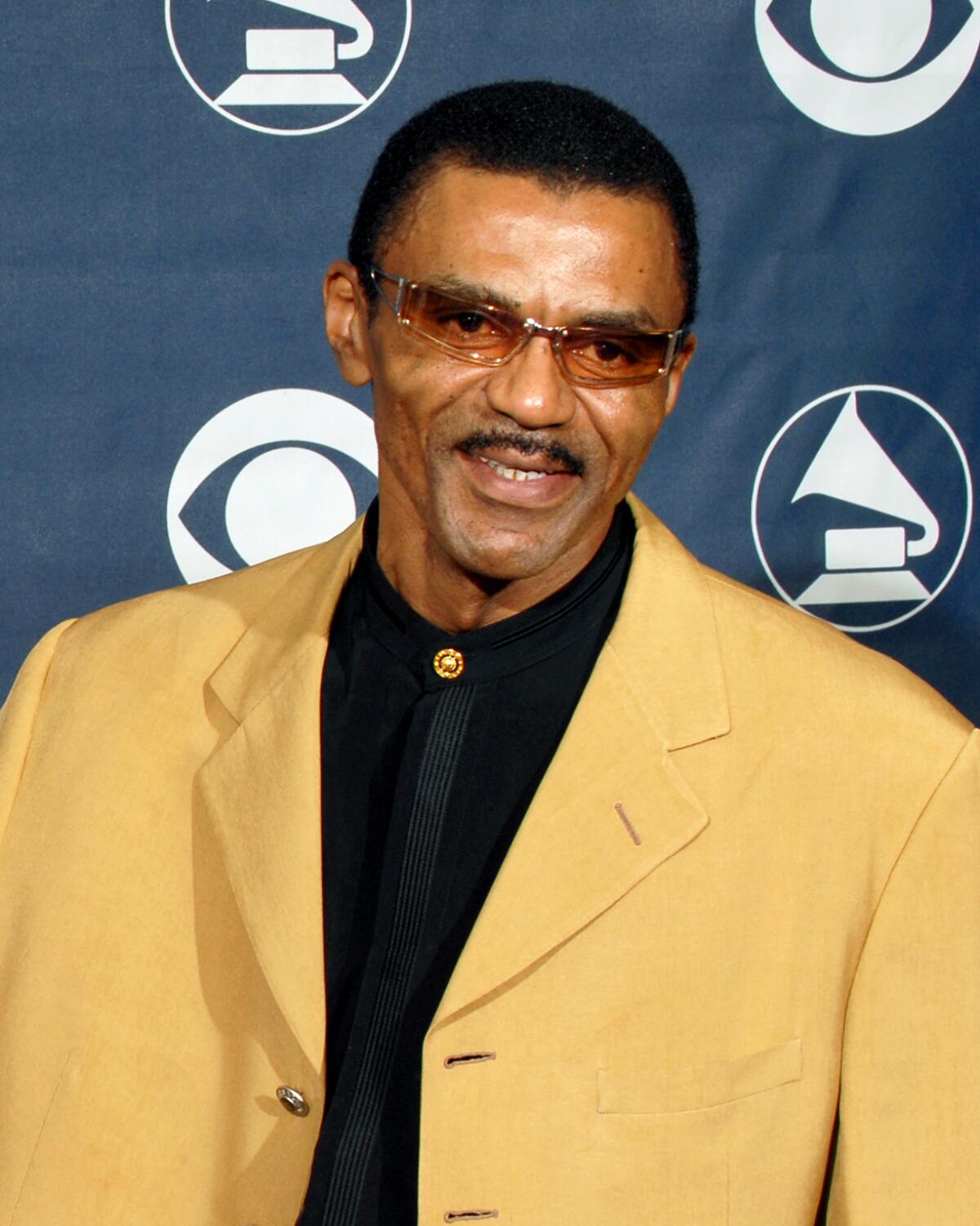 A smiling Ike Turner Jr. wears a yellow jacket and tinted rectangular glasses.