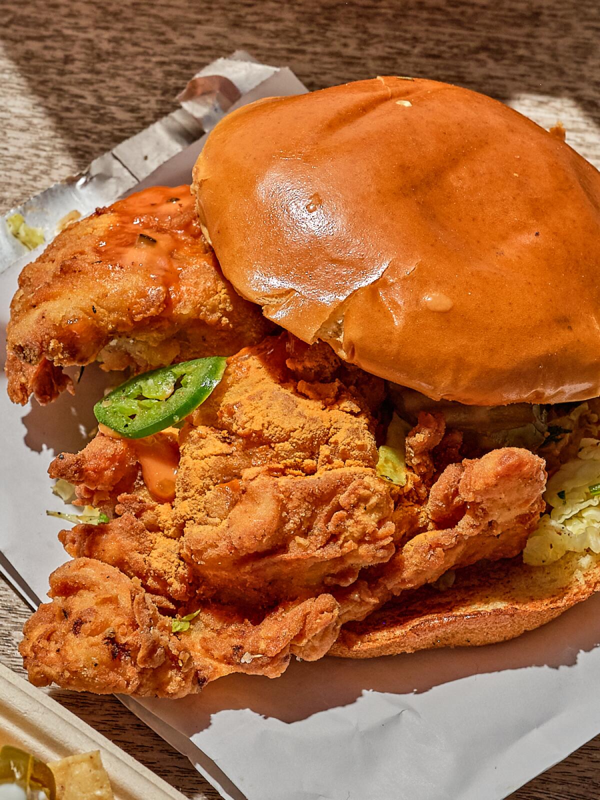 Closeup of a sandwich with hamburger bun, fried chicken and a jalepeo slice.