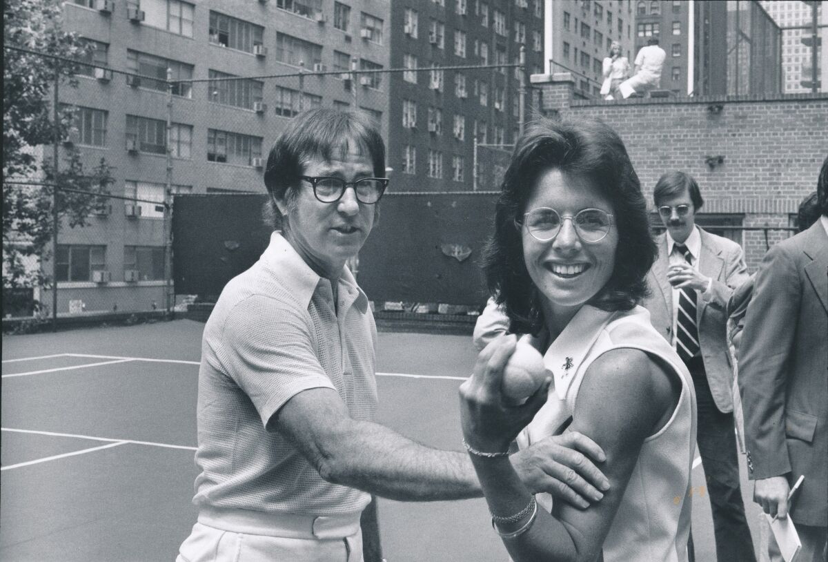 Bobby Riggs grabs Billie Jean King's upper arm on the tennis court in a 1973 black-and-white photo.