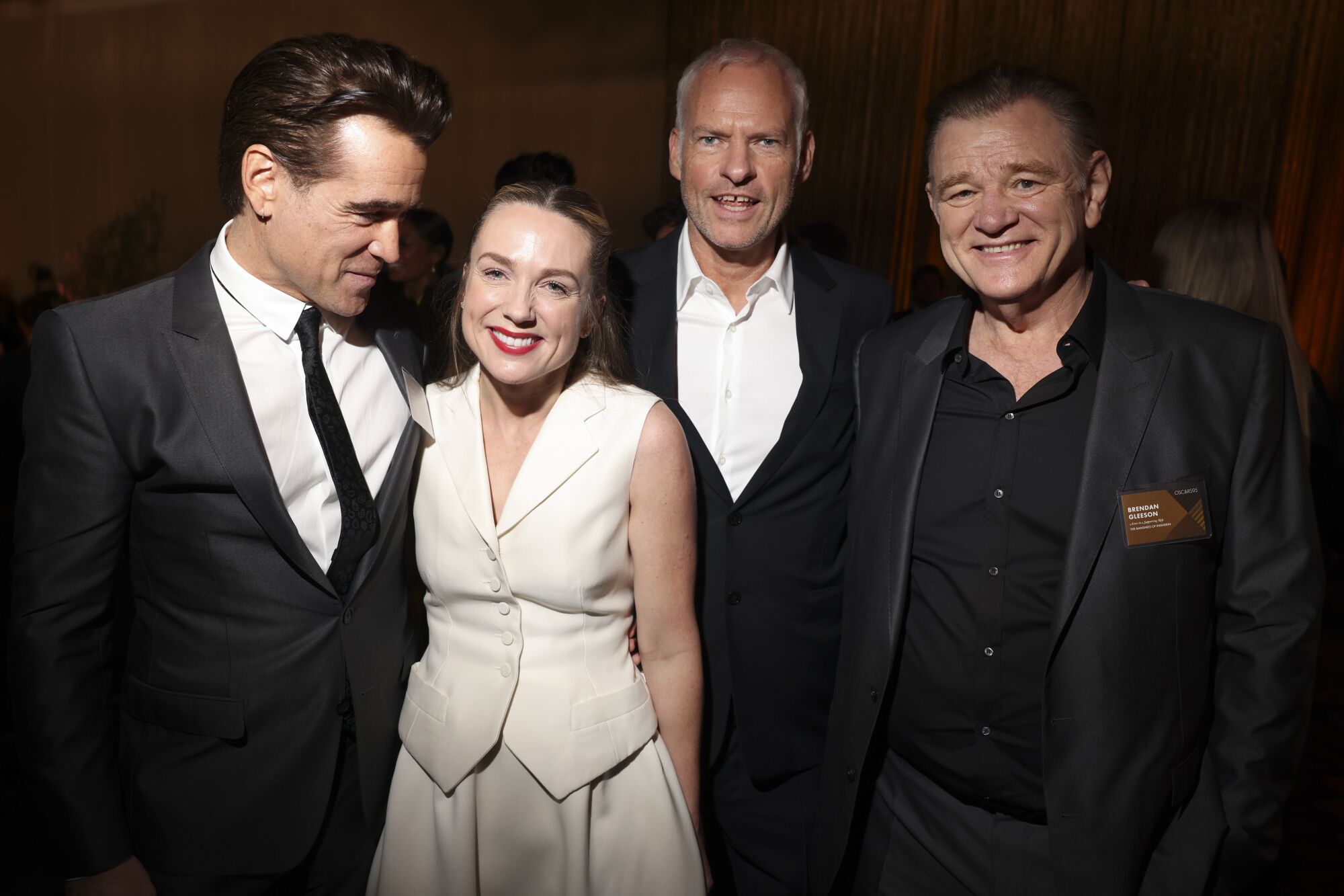 Three men in dark suits and a woman in a white sleeveless top. 