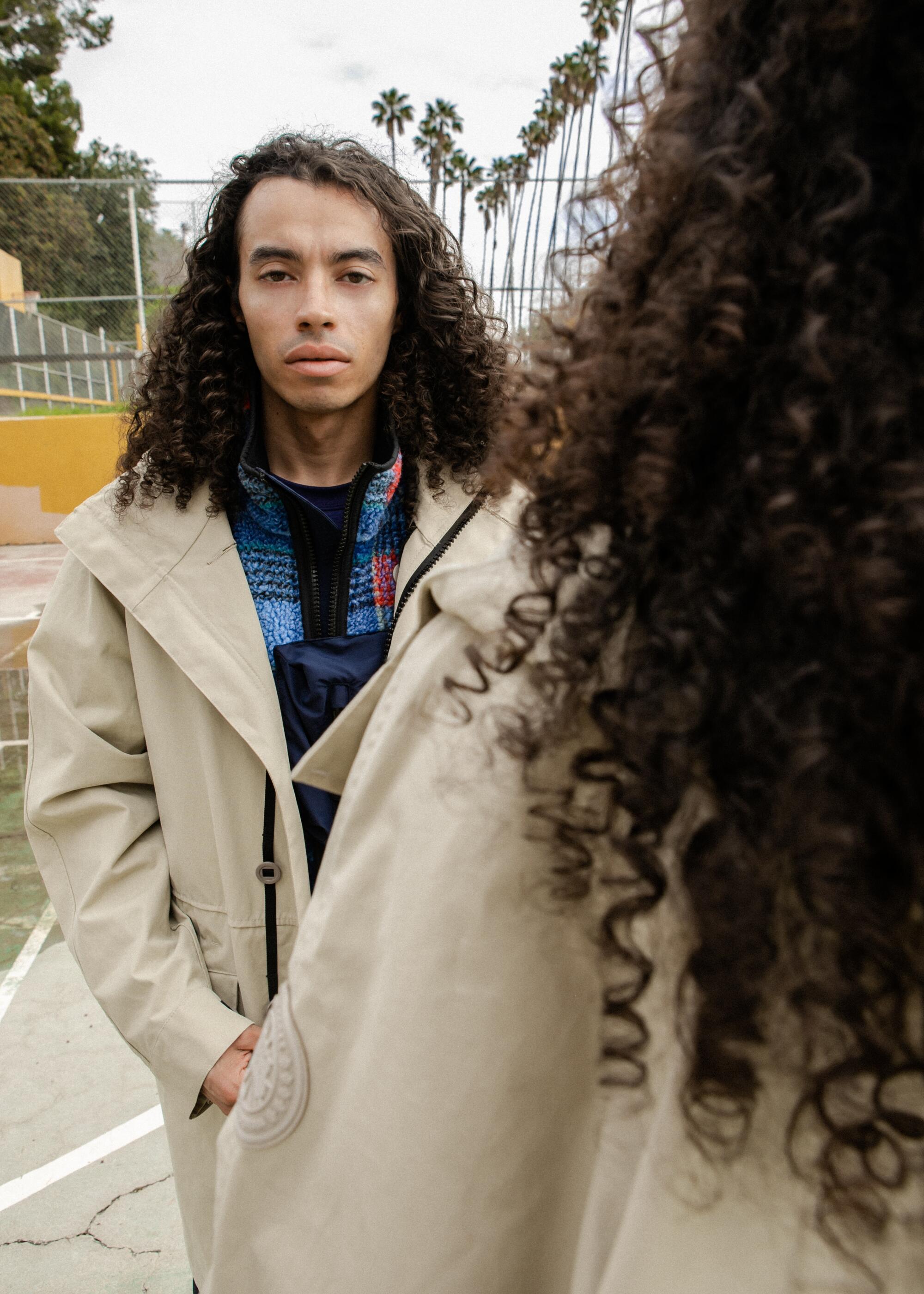 Model stares at camera in trench coat at Lincoln Heights basketball court.