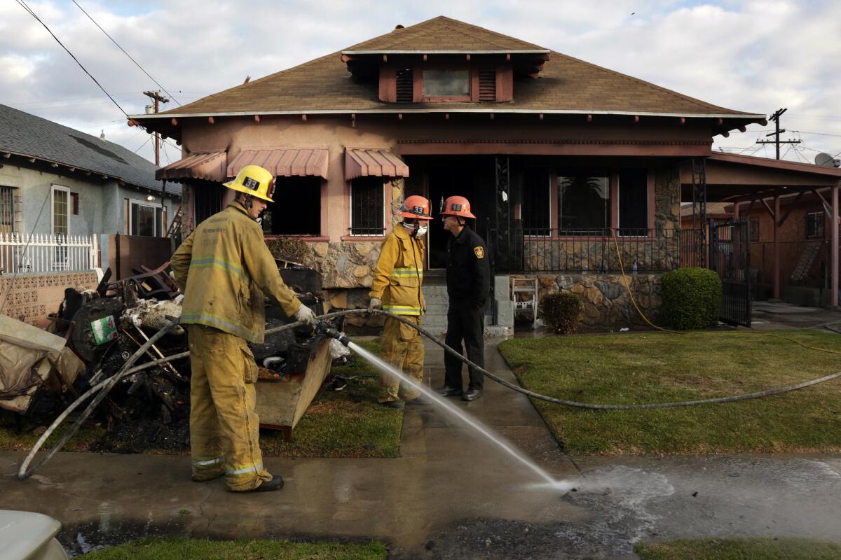 A firefighter hoses down a sidewalk in front of a South Los Angeles house where a woman died of smoke inhalation after being rescued from a fire.