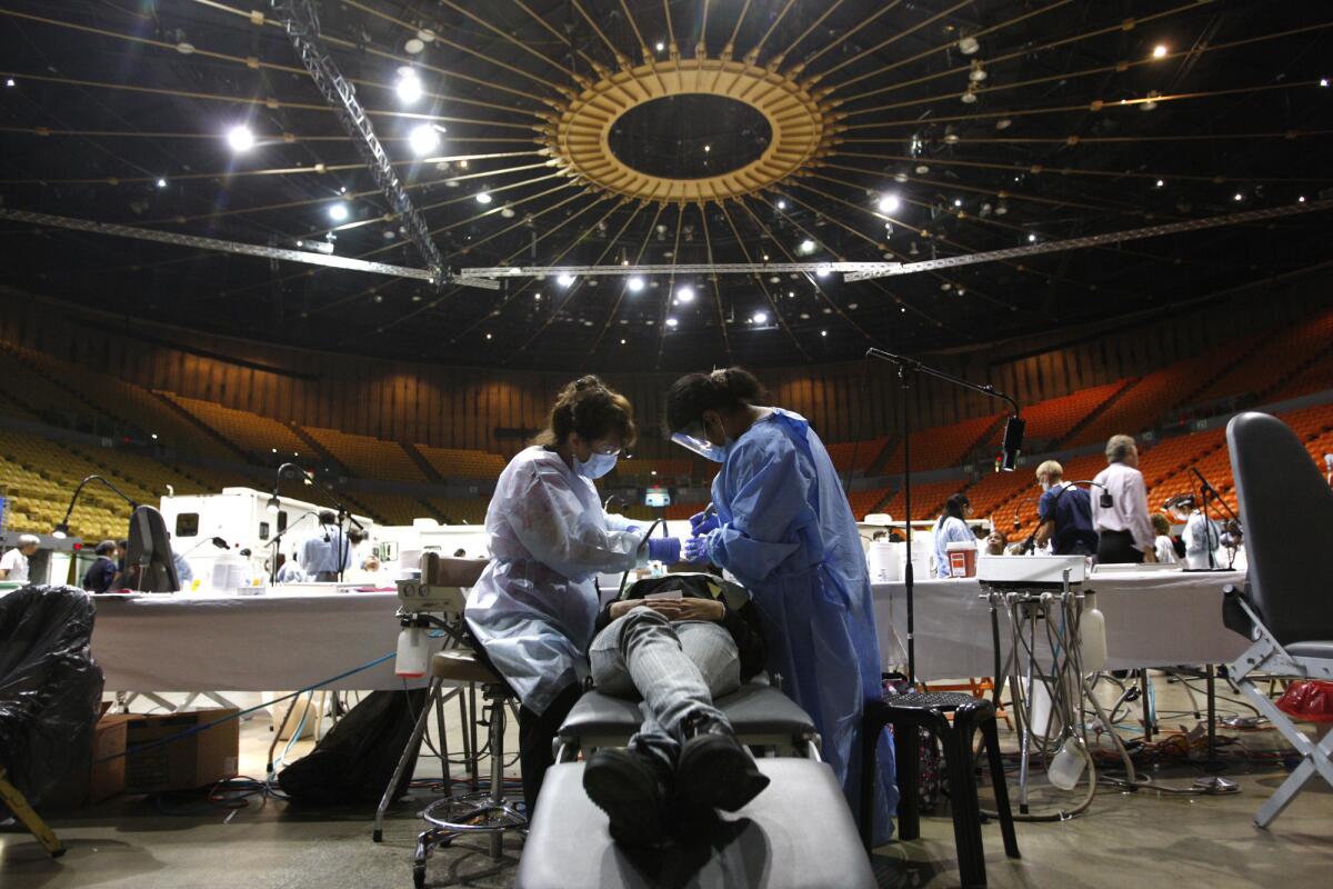 Dental hygienist Mary Kay Alexander, left, and dental assistant Erika Bravo work on a patient during the final day of the Remote Area Medical health fair and clinic at the Forum in Inglewood.