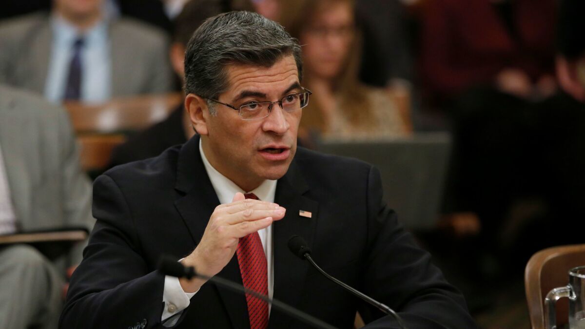 California Atty. Gen. Xavier Becerra speaks into a small microphone while seated at a hearing