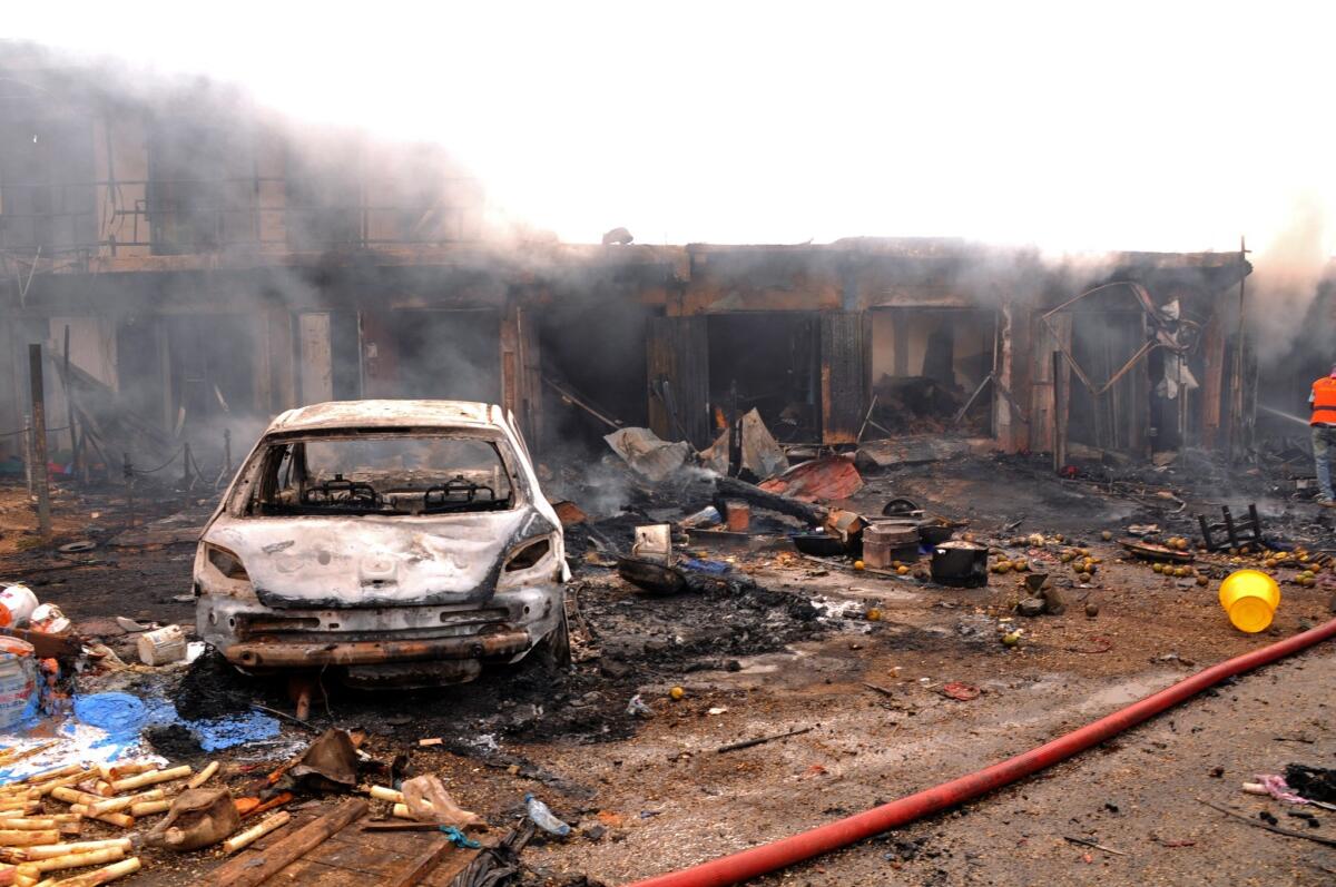 The wreckage of a vehicle stands in front of burning shops after a bomb exploded at a market in the central Nigerian city of Jos.