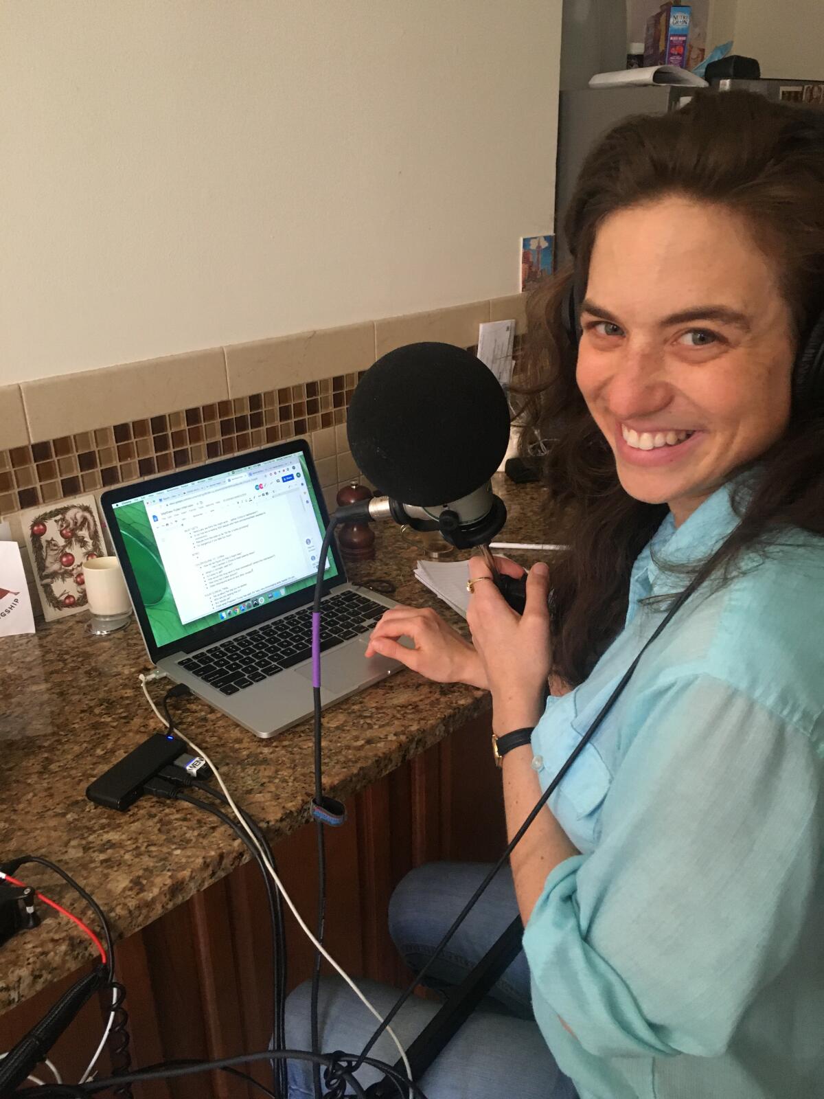 A woman seated at a desk with an open laptop and a microphone.