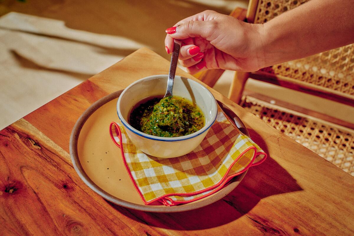 A hand spoons Sichuan chimichurri sauce out of a small white bowl