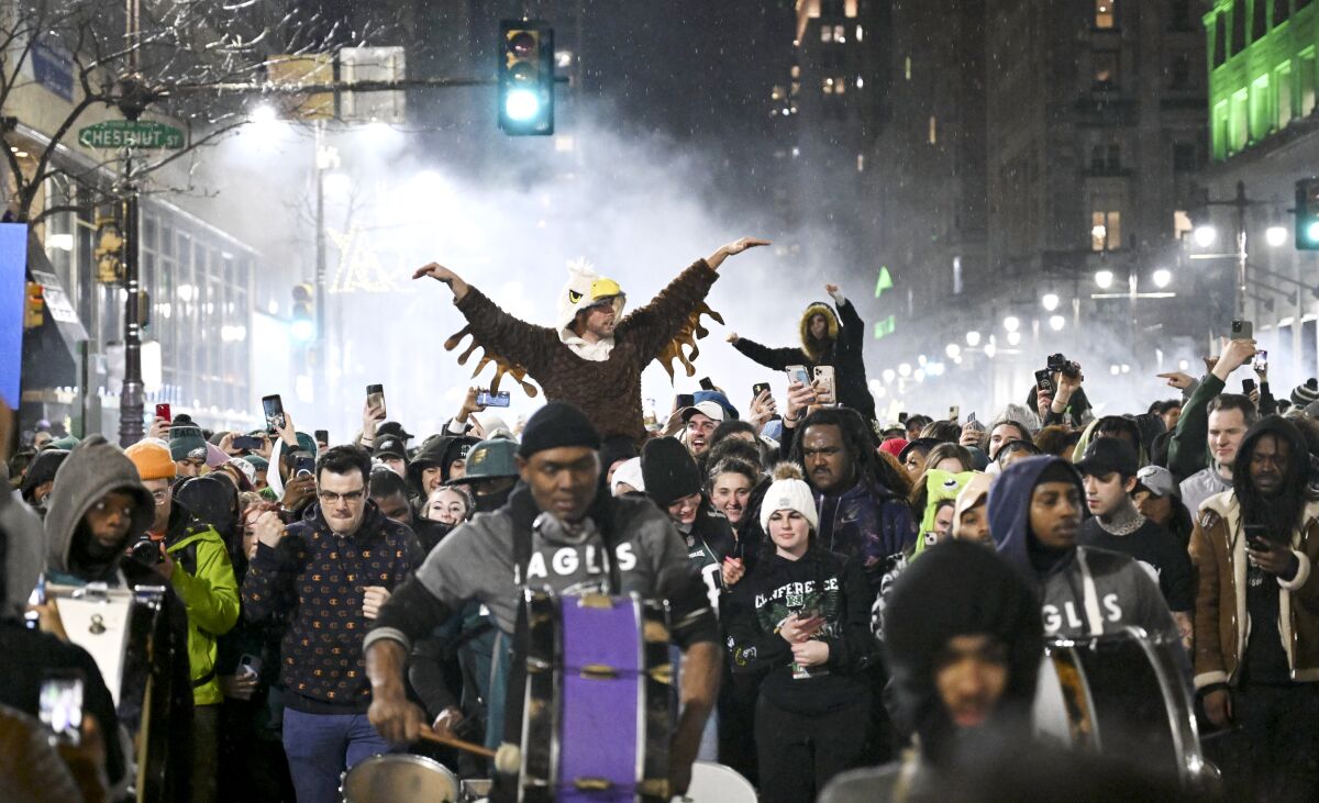 A person in an eagle costume rides someone's shoulders amid a crowd of people in the street