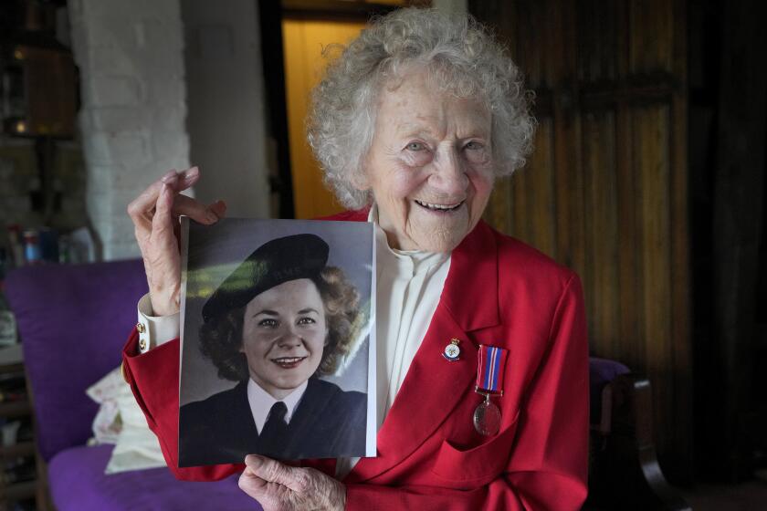 Dorothea Barron who was a serving Wren at the time of D-Day, holds up a photograph of herself in uniform during WWII, at her home near Sawbridgeworth, in England, Tuesday, May 7, 2024. D-Day, took place on June 6, 1944, the invasion of the beaches at Normandy in France by Allied forces during World War II. (AP Photo/Kirsty Wigglesworth)