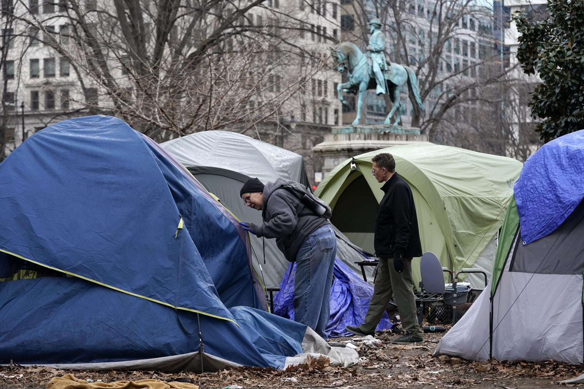 Homeless advocates check inside tents near a statue and buildings.