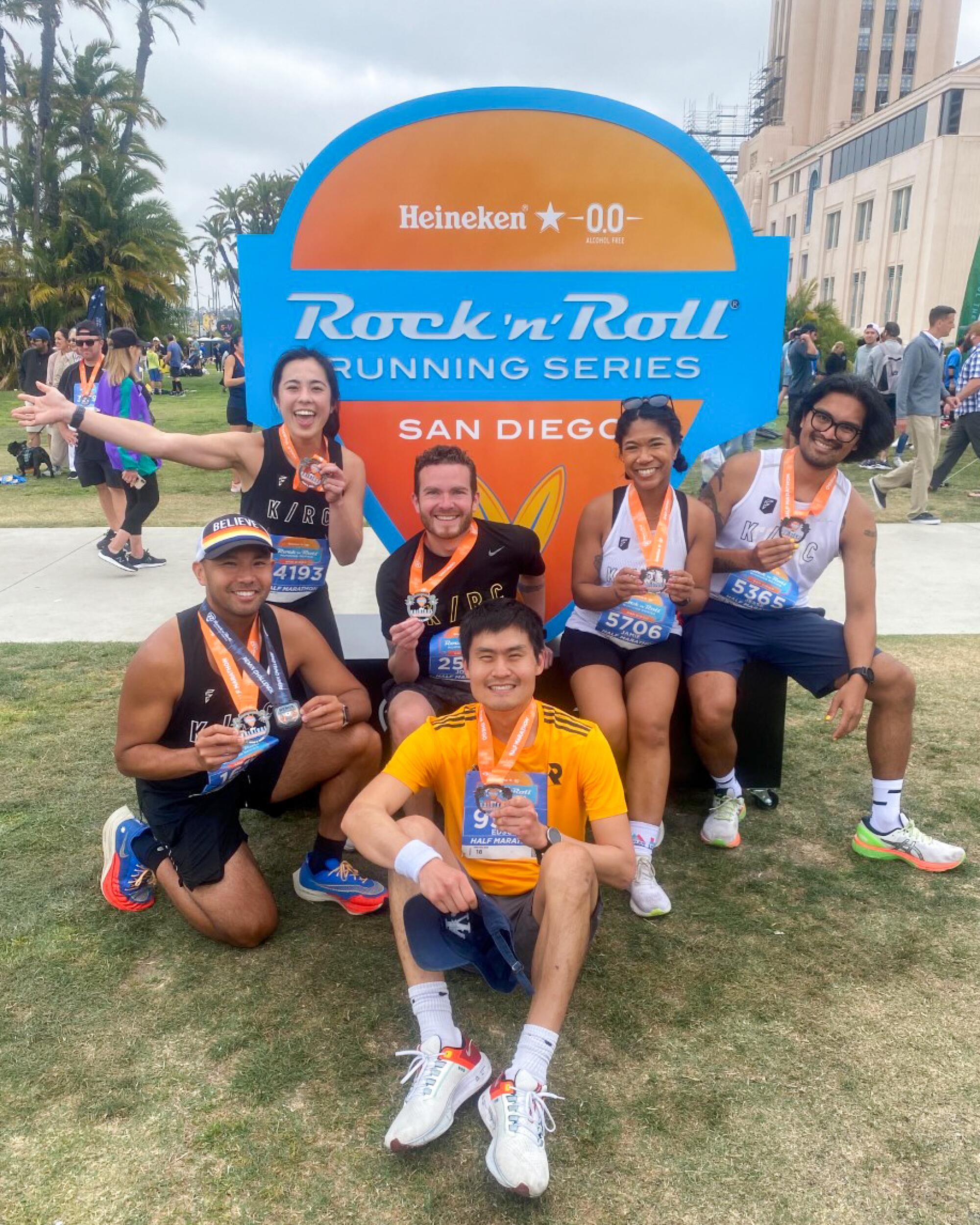A group of people from a run club pose in front of a Rock and Roll Running Series sign.